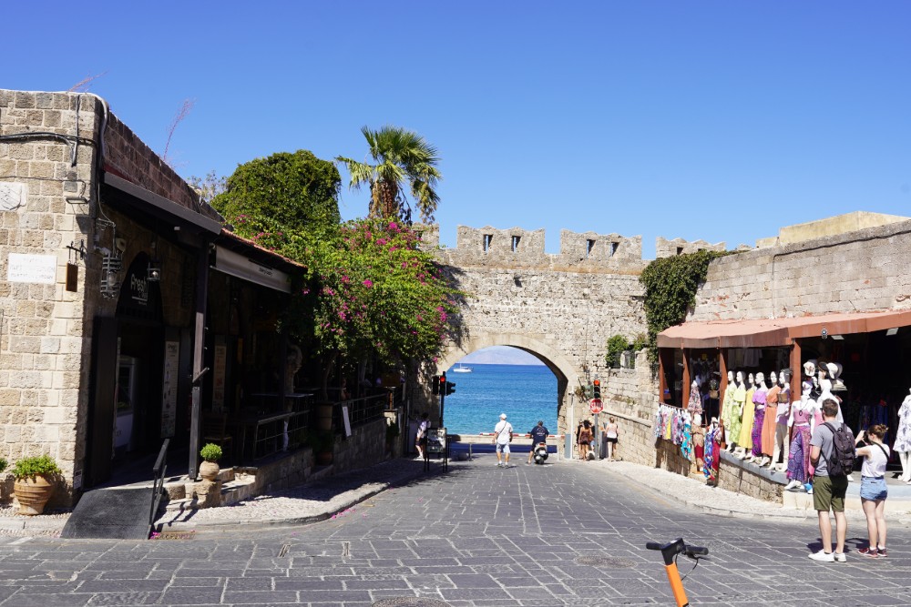Eine Straße auf Rhodos mit einem steinernen Torbogen und Blick auf das Meer.