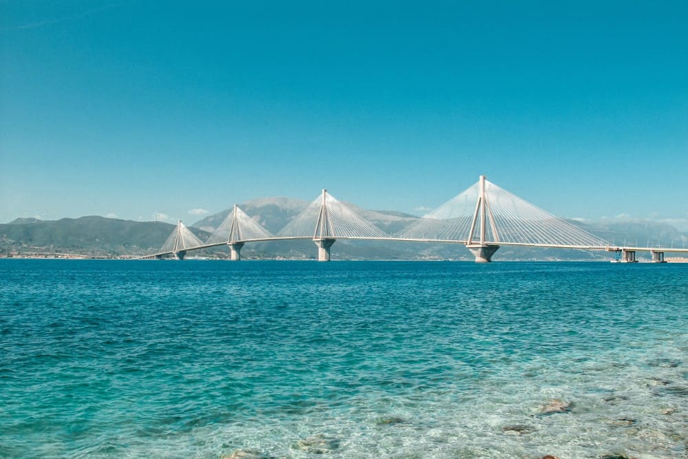 Eine große Brücke über das Wasser mit Bergen im Hintergrund, eine der Sehenswürdigkeiten von Patras.